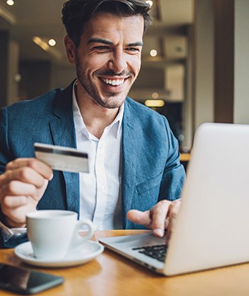 Man sitting in front of his labtop with a cup of coffee and credit card in hand